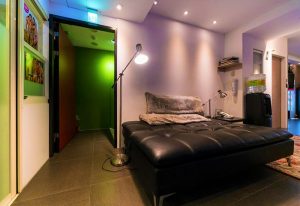 Gs Gay Hotel interior. Lounge area with black leather couch, lamps, and colorful walls. Gay-friendly hotel design.