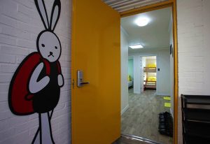 Gay-Friendly Guest House DODAMi interior. Yellow door, bunny art, and view into a room with bunk beds. Gay travel lodging.