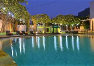 Pool at HARRIS Hotel Tebet, a gay-friendly hotel. Evening view with lounge chairs, trees, and reflections in the water. Jakarta, Indonesia.