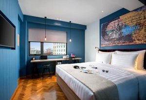 Hotel G Yangon's gay-friendly room. Blue walls, wooden floors, a bed with white linens, and a desk by the window. Art on the wall.