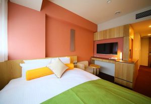 Hotel Gracery Shinjuku gay-friendly hotel room. Modern design, bed with colorful pillows, TV, and wooden furniture. Ideal for gay travelers.