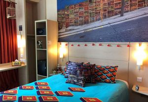 Ibis Hong Kong Central & Sheung Wan Hotel room. Gay-friendly hotel with colorful decor, bed, and Hong Kong street scene mural.