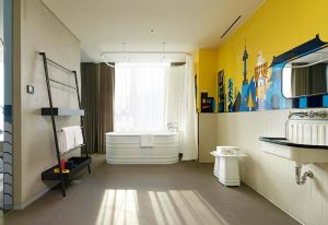 L7 Myeongdong by LOTTE hotel bathroom. Features a tub, yellow wall with Seoul skyline art, and a modern sink. Gay-friendly hotel in Seoul.
