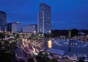 Pullman Jakarta Indonesia, gay-friendly hotel. Night view of the city with a fountain, skyscrapers, and traffic. Gay travel advice.