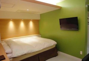 Shinjuku City Hotel N.U.T.S Tokyo room. Gay-friendly hotel with a bed, TV, and green walls. Modern design for LGBTQ+ travelers in Shinjuku, Japan.
