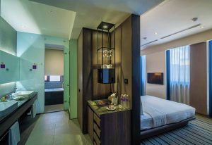 WESTGATE Hotel room with modern design. Bathroom with double sink, bedroom with TV, bed and blue curtains. Gay-friendly hotel for gay men travel.