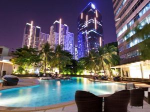 Wyndham Casablanca Jakarta gay-friendly hotel pool at night. Modern buildings, palm trees, and lounge chairs create a relaxing atmosphere.