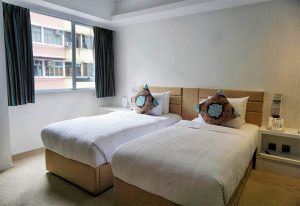 The Figo, gay-friendly hotel room with two twin beds, headboards, and decorative pillows. Window with curtains. Ideal for gay men travelers.