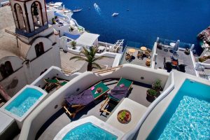 Aperto Suites Adults Only, gay-friendly hotel. View of Santorini's white architecture, Aegean Sea, private pools, and sun loungers.