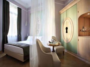 Chateau Monfort Hotel room interior. Gay-friendly hotel with bed, chairs, table with tea set, and cabinet with keyhole design. Elegant, romantic.