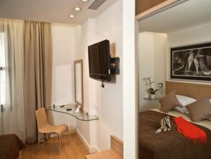 Gay-Friendly Chic Hotel room. Modern design with TV, glass desk, and a glimpse into the bedroom area. Ideal for gay men travelers.