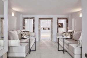 Cosmopolitan Suites gay-friendly hotel interior. White sofas, round tables, and stone doorways leading to a bedroom. Luxury travel vibe.