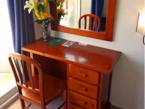 Desk at Hostal Residencia Molins Park, a gay-friendly hotel. Wood desk, chair, mirror, flowers, and blue curtains in the room.