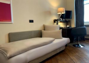 Hotel Deutsche Eiche's gay-friendly room: daybed with pillows, desk, chair, lamp, TV, and wood floors. A comfortable stay for gay travelers.