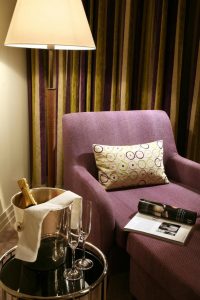 Rocco Forte The Charles Hotel room detail. Champagne bucket, glasses, and magazine on a purple chaise lounge. Gay-friendly hotel.
