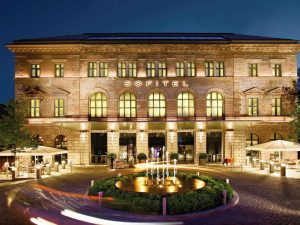 Sofitel Munich Bayerpost Hotel exterior at night. Gay-friendly hotel with fountain. Luxury travel for gay men in Munich.