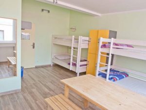 Dorm room at Wombats City Hostel Munich, a gay-friendly hotel. Bunk beds, lockers, table, and bench seating create a budget-friendly travel space.