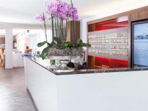 Carathotel Munchen City's reception area. This gay-friendly hotel features a sleek white counter with orchid centerpiece. Modern, welcoming design.