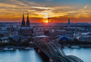 Cologne skyline at sunset. Gay travel tips: Explore this hot gay city! View of the Cathedral, bridge, and Rhine River. Visit Cologne this year!