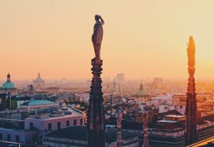 Milan skyline at sunset from Duomo rooftop. Gay travel guide to find cheap gay hotels in Milan's gayborhood. Milano travel tips.