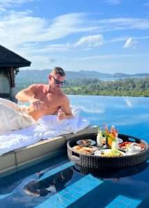 Gay travel: Man relaxes by private pool villa at The Pavilions Phuket, a gay-friendly beach hotel, enjoying breakfast with a scenic view.