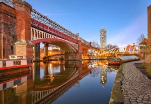 Manchester travel: Canal view with bridges and boats at dusk. Gay travel advice for exploring Manchester's waterways.