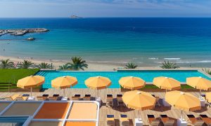 Beachfront gay hotel in Benidorm. Pool view with umbrellas, sea, and beach. A great place for gay travelers to relax and enjoy the sun.