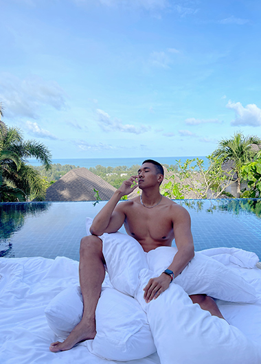 Gay honeymoon at The Pavilions Phuket: Man relaxes on a bed by the pool villa, enjoying the tropical view. Top gay honeymoon destination.