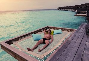 Gay Maldives: Man relaxes on a hammock over turquoise water at a top-ranked gay couples resort. First timer's guide to Maldives.