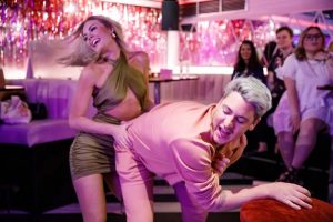 Fun at Tonight Josephine Clapham, a London gay bar. Woman in green dress playfully spanks a man in pink, with other patrons in the background.