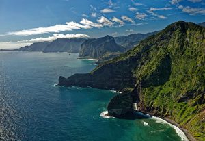 Gay Madeira Travel Guide: Scenic coastline view. Lush green cliffs meet the blue ocean under a partly cloudy sky, perfect for gay travel adventures.