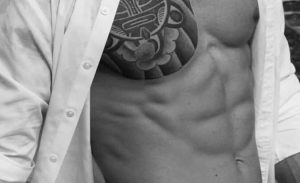 Torso of a fit man with tattoo, shirt open. Massage By Bret, gay massage spa. Male physique, black and white. Gay travel advice.