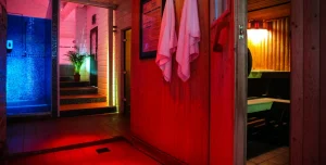 Interior of a gay sauna, sailors sauna, with red walls, towels, a shower room with blue lighting, and a traditional sauna room.