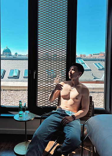 Gay man in Berlin hotel near gay bars. Shirtless man in The Weinmeister Berlin-Mitte with city view. Cheap city hotel for gay travel.