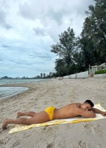 Gay Hua Hin travel: Man in yellow swim briefs lounges on the beach at The Standard, a beachfront pool villa. Number one gay destination.