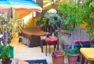 Cozy outdoor seating at Sami's Bar, Athens. Lush greenery, colorful umbrella, and relaxed atmosphere. Gay travel guide recommendation.