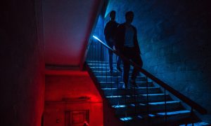 Two men on stairs in a Vienna gay cruise club. Red and blue lights illuminate the scene. Best and most popular gay club.