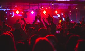 Crowd at a Prague gay club, arms raised, bathed in red light. Top must-go dance clubs for gay men in Prague. Gay travel advice.
