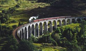 Steam train on Glenfinnan Viaduct, Scotland. Best country hotels offer scenic views. Gay-friendly hotels in Scotland for memorable travel.