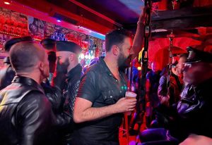 Le Mensch Paris: Gay men in leather attire at a bar. Fetish scene with men in caps, vests, and harnesses. Nightlife in Paris for gay travelers.