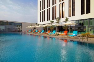 Aloft Me'aisam Dubai's pool, a gay-friendly hotel. Colorful lounge chairs line the pool. Modern architecture, Dubai hotel.