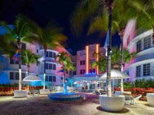 Axel Beach Miami gay-friendly hotel at night. Haddon Hall with neon lights, palm trees, fountain, and outdoor seating. Gay travel destination.