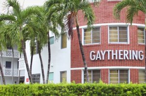 Gaythering: A gay-friendly hotel with palm trees. The building has a red brick section with the hotel's name and a white section.