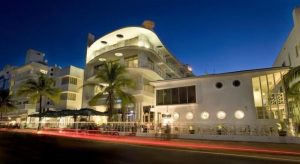 Strand Ocean Drive Suites, a gay-friendly hotel. Art Deco building at night with palm trees. Ideal for gay men's travel to Miami Beach.
