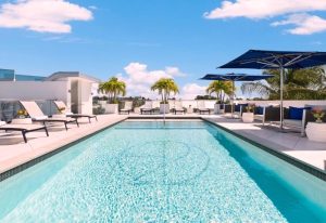 Rooftop pool at a gay hotel in Key West. Lounge chairs, umbrellas, and palm trees surround the pool, offering a relaxing and luxurious vacation spot.