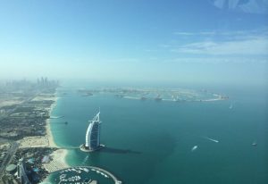 Aerial view of Dubai, a gay travel destination, featuring the Burj Al Arab hotel, coastline, and Palm Islands under a clear blue sky.