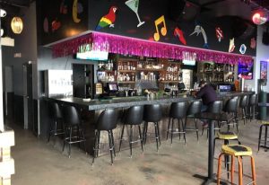 Gramps gay bar: Interior shot of the bar area with stools, a bartender, and colorful decorations on the wall. Gay travel advice.