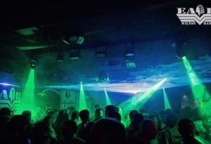 Inside The Eagle Wilton Manors gay bar. A crowd of men dance under green lights and a disco ball. Wilton Manors nightlife scene.