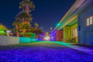 Night view of CCBC Resort Hotel, a gay men's resort. Colorful buildings, palm trees, and a starry sky create a vibrant, welcoming atmosphere.