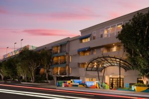 Le Parc at Melrose, a gay-friendly hotel. Exterior view of the hotel entrance at dusk, showcasing its modern architecture and colorful accents.
